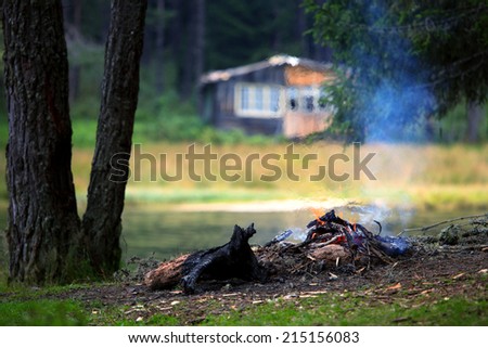 camp fire near lake in autumn time with wooden villa in background