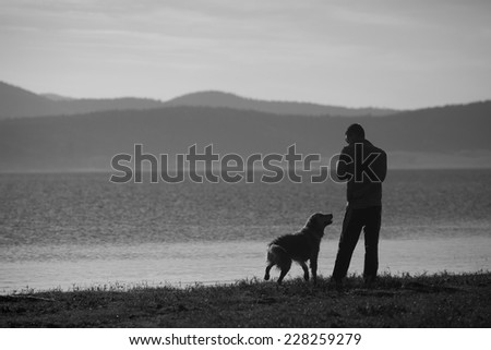 man and dog near high mountain lake in sunset time, black and white landscape