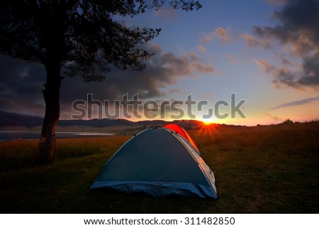 recreation area and camp with tent, sunset time with rising sun near high mountain lake, HDR technique used