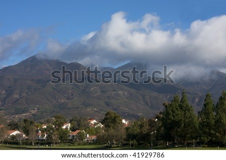 Mountain landscape with low clouds and residential homes at bottom of hills