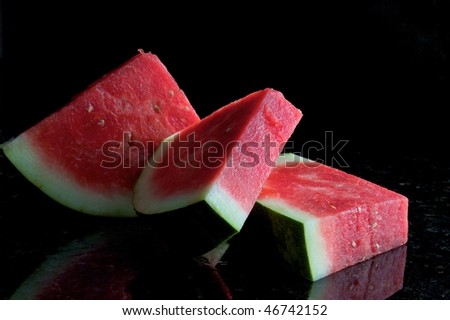 Three slices of watermelon against black background with reflections