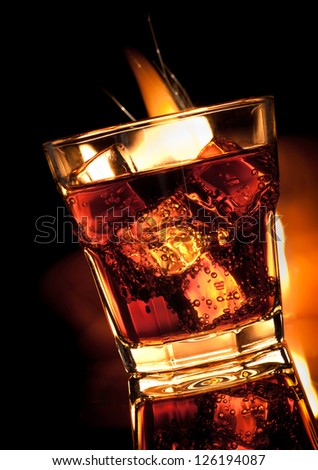 cola with whiskey in glass and fire on black