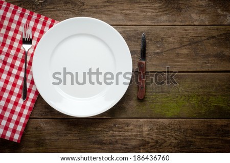 Empty white plate on wooden table over red grunge background