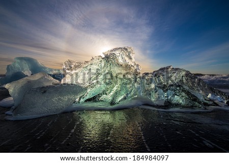 Ice block from Jokulsarlon melting slowly on Breidamerkursandur beach, sun is lighting the ice from behind