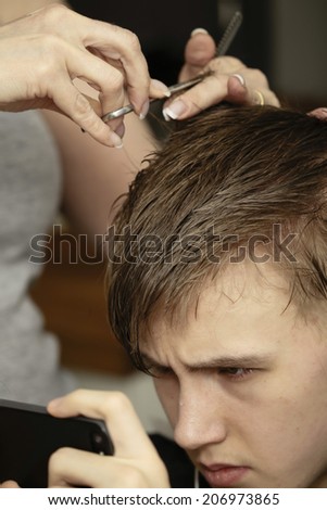 Young man texting on his smartphone while having his hair cut