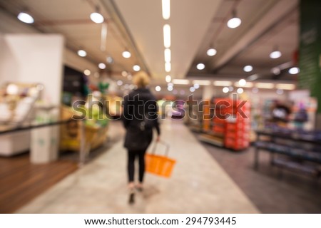 Out of focus shot from behind of a woman walking inside a supermarket starting her grocery shopping trip