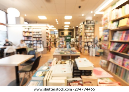 Out of focus shot from inside of a bookstore with cafe, books in shelves and on tables, customers reading magazines and drinking coffee to the left