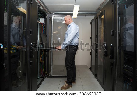 Computer specialist working on servers in a server room, looking at computer display in one of the cabinets