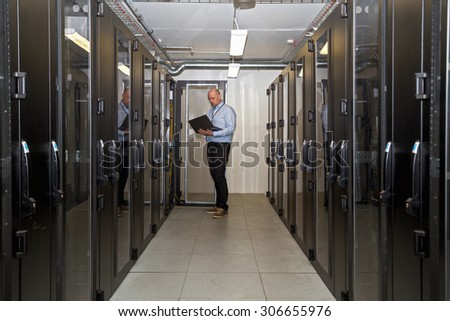 Server administrator working late on updating servers in a server room outside office hours, holding a laptop to check on progress