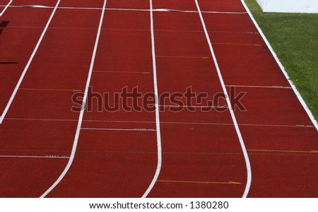 Straight red running track with white dividing lines part of grass visible
