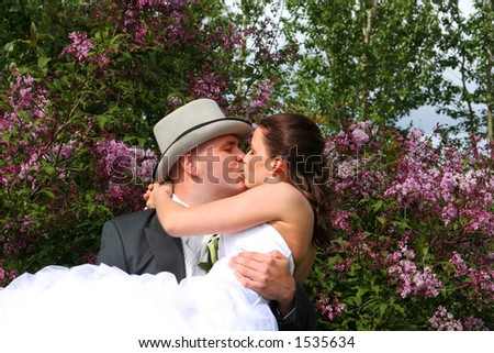 bride and groom kissing, groom holding bride standing on front of a tree with intense purple colored flowers