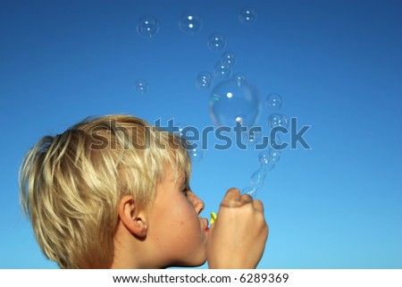 small boy blowing bubbles against a deep blue sky