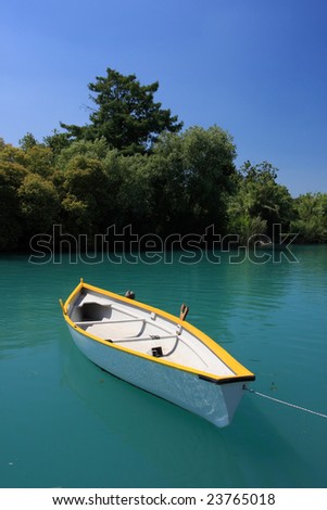 A clean white boat floating on a deep green river, trees and blue sky in background