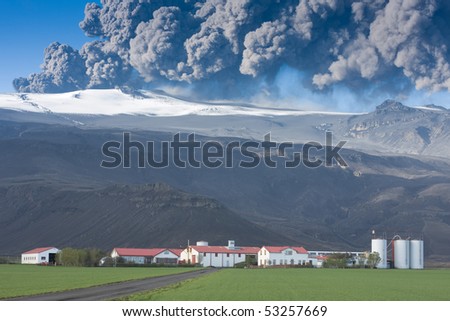Eyjafjallajokull in Iceland erupting, ash plume against blue sky above the farm Thorvaldseyri, green fields in the foreground