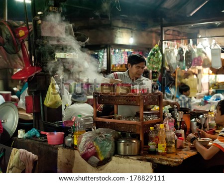 SIEM REAP, CAMBODIA - DEC 22, 2013: Unidentified Khmer man selling traditional food at marketplace on December 22, 2013 in Siem Reap, Cambodia. Street food cooking and selling is a local tradition