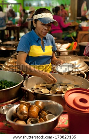 SIEM REAP, CAMBODIA - DEC 22, 2013: Unidentified Khmer woman selling traditional food at marketplace on December 22, 2013 in Siem Reap, Cambodia. Street food cooking and selling is a local tradition