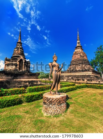 Ancient architecture of Buddhist temples in Sukhothai Historical Park. Statue of walking Buddha at Sa-Si Temple under blue sky. Thailand