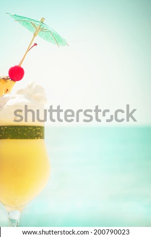 Pina colada cocktail with fruits and umbrella decoration at tropical ocean beach. Vintage style, hipster colors image with copy space for party invitation text