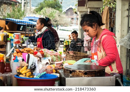 LUANG PRABANG, LAOS - DEC 8: Unidentified girl helps her mother to sell traditional asian food at street marketplace on Dec 8, 2013 in Luang Prabang, Laos