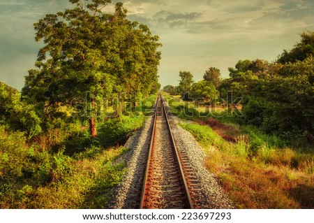 Railway track crossing rural landscape under evening sunset sky. Travel concept in vintage hipster style