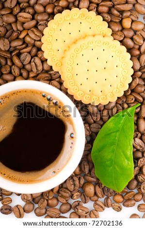 Coffee beans, green leaf of coffee plant with cookies and cup of coffee. Focus on beans
