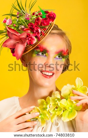 Beautiful young girl with creative flower cap and orchid flower. Artistic makeup with long feather artificial eyelashes and bright colorful eyeshadow