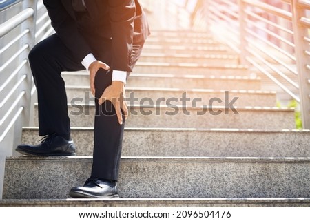 Businessman in a suit have the sore pain and painful knee problem expression and walk up and down on the stairway during go to office. Health care concept. Foto stock © 
