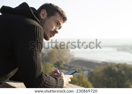 Handsome Man Holding Mobile Phone Outdoor On River Bank