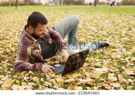 Man With Beard Laying Down In Autumn Leaves Using Laptop Computer