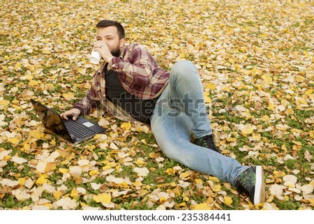 Urban Man Laying Down In Autumn Falling Leaves Using Laptop Computer Outdoor