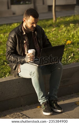 Man Using Laptop Computer and Drinking Coffee From To Go Cup