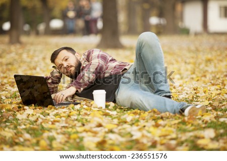 Man Laying Down In Autumn Leaves Using Laptop Computer