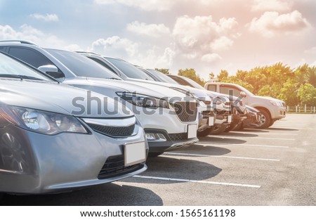 Front view car parking in asphalt parking lot in a row with white cloud and blue sky background. Outdoor parking lot with fresh ozone and green environment of travel transportation technology concept