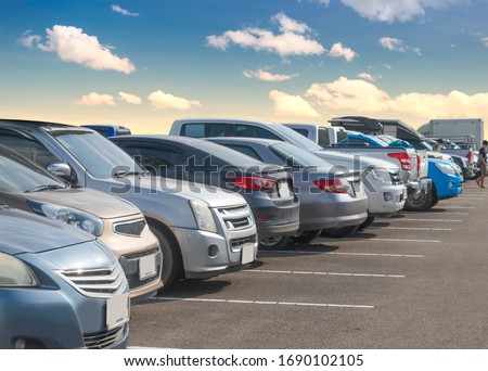 Car parking in large asphalt parking lot with white cloud and blue sky background. Outdoor parking lot with fresh ozone and green environment of transportation and modern technology concept