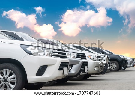 Cars park in asphalt parking lot in a row with cloudy sky background in nature. Outdoor parking lot with fresh ozone, green environment of transportation and technology concept
