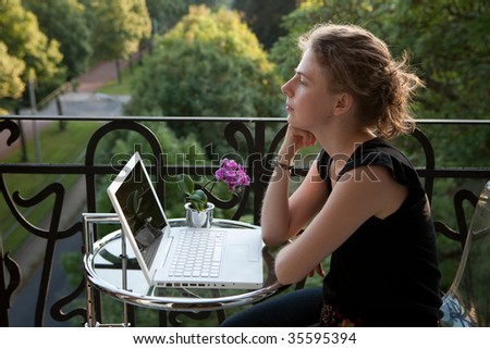 smiling young woman writing on a white modern laptop computer on a balcony in art nouveau