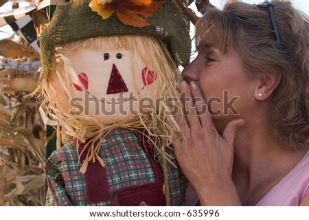 a pretty woman whispers into a scarecrows ear.