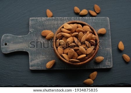 Almonds nuts  in a round wooden cup on a black shabby chic board on a black schiffer  background.Nuts and seeds. .Healthy fats.Heap Almonds shelled  nut closeup.Tasty organic snack 