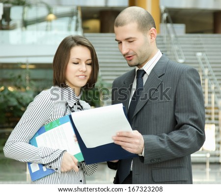 Portrait of two business people standing in the office looking into folder with business plan