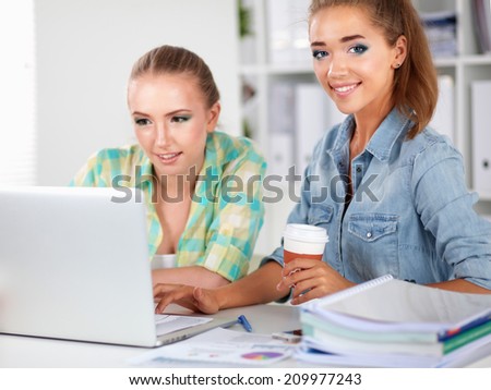 Two women working together at office, sitting on the desk
