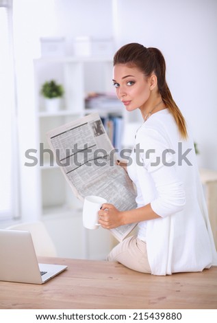 Cute businesswoman holding newspaper sitting at her desk in bright office