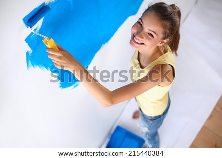 Happy beautiful young woman doing wall painting, standing on ladder