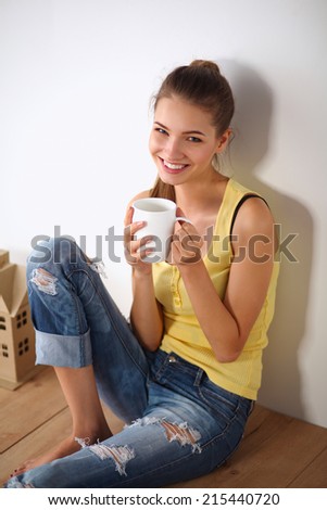 Portrait of female painter sitting on floor near wall after paintingand holding a cup
