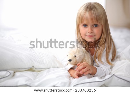 Little girl with teddy bear lying on the bed at home , isolated