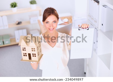 Portrait of female architect holding a little house, standing in office