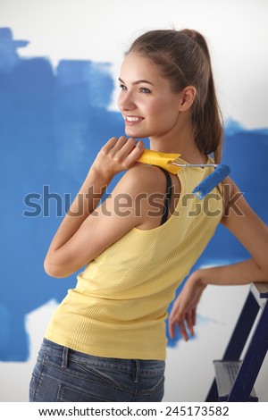 Beautiful young woman doing wall painting, sitting on ladder