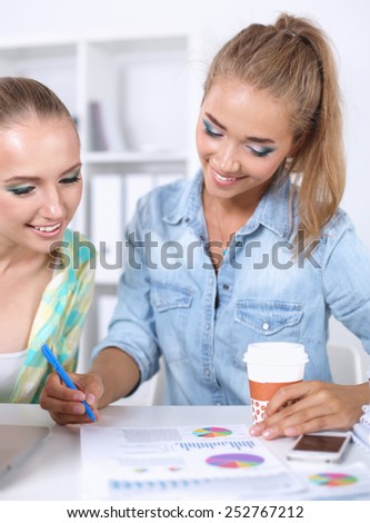 Two women working together at office, sitting on the desk.