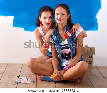Two beautiful young woman doing wall painting, sitting .