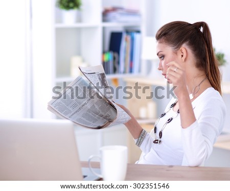 Cute businesswoman holding newspaper sitting at her desk in office .