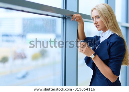 Businesswoman standing against office window holding documents in hand
